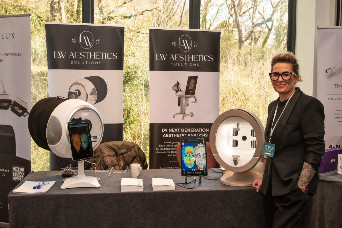 Louisa Webb at an industry exhibition with LW Aesthetics Solutions banners and skin analysis devices